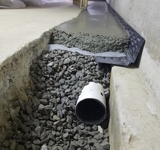 a trench cut in basement floor in cranberry township, pittsburgh, pipe laid in and gravel with conctete top dressing to capture moisture and dtrain it out of the building. 