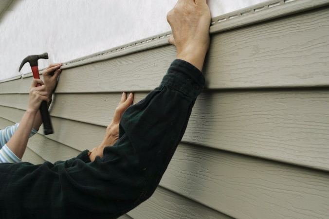 A Pit Pro Handyman installing vinyl siding, color tan, on a residential stucco wall. 