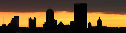 Image of a golden sky with the sunsetting and the Pittsburgh Pennsylvania skyline in the foreground. There are ten buildings visible including the iconic PPG castle building. 
