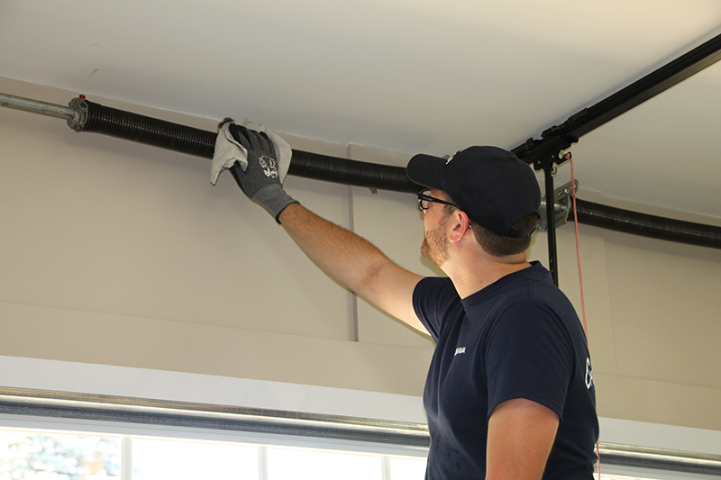 Photo of Pit Pro Handyman cleaning the springs on a garage door. Using gloves to wipe the spring prior to lubrication. 